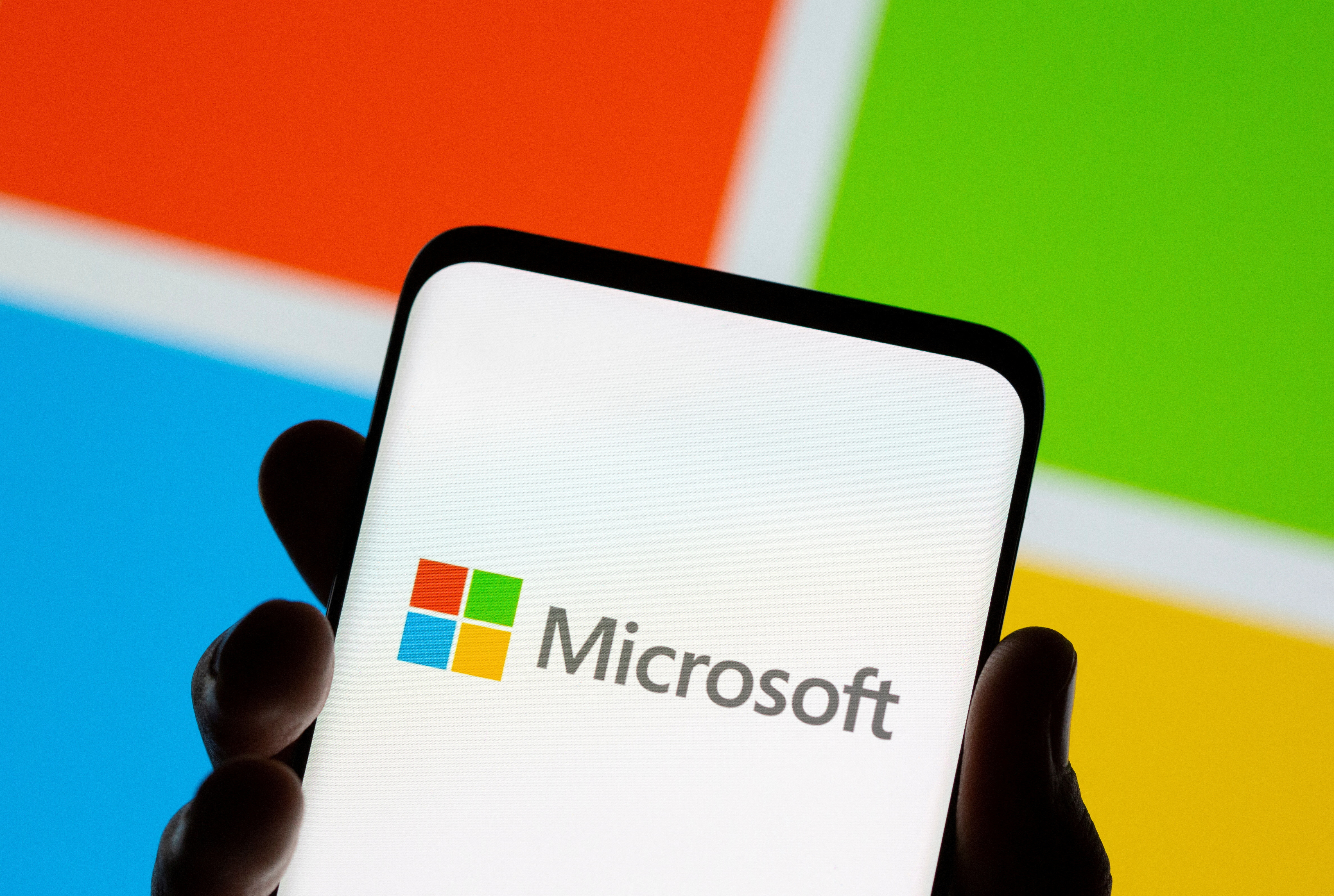 يظهر الهاتف الذكي أمام شعار Microsoft المعروض في هذا الرسم التوضيحي