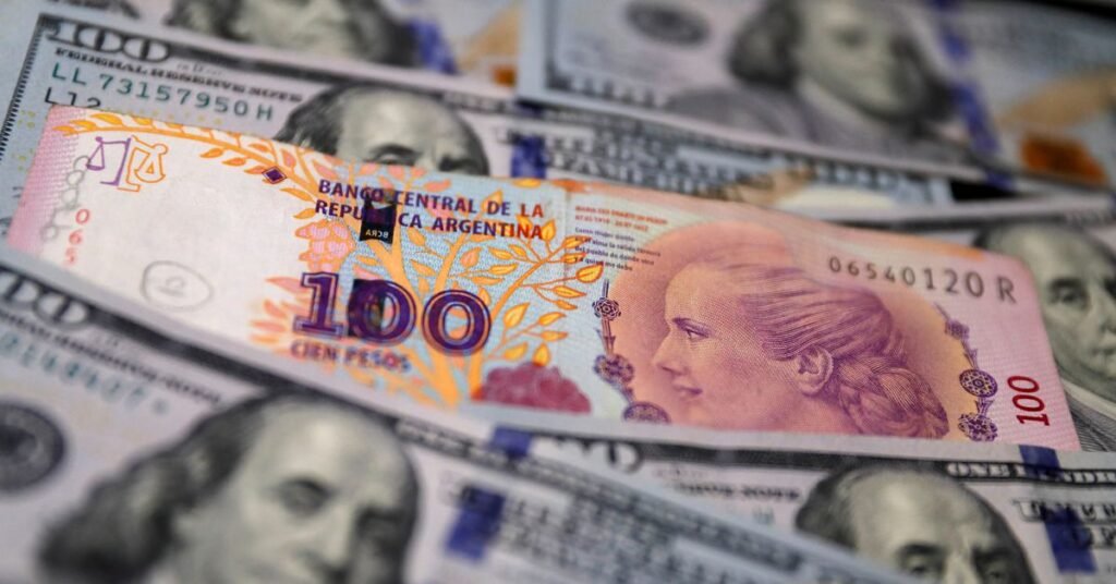 A one hundred Argentine peso bill sits on top of several one hundred U.S. dollar bills in this illustration picture