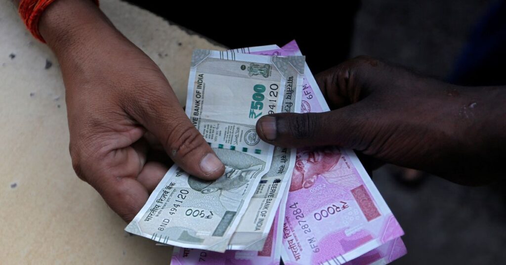 A customer hands Indian currency notes to an attendant at a fuel station in Mumbai