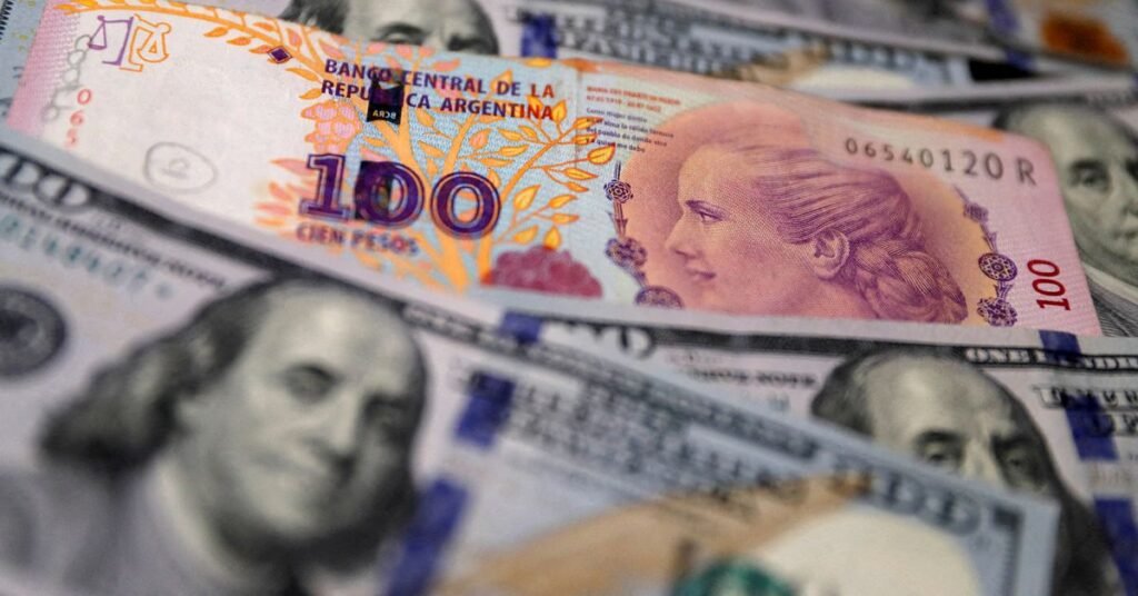 A one hundred Argentine peso bill sits on top of several one hundred U.S. dollar bills in this illustration picture