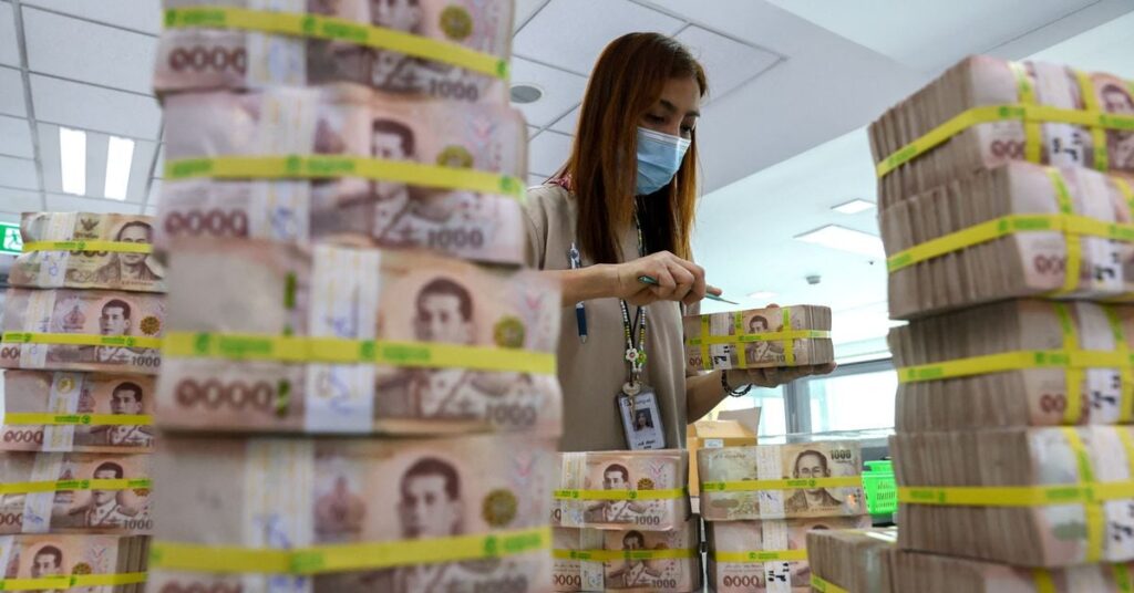 A bank employee gathers Thai baht notes at a Kasikornbank in Bangkok