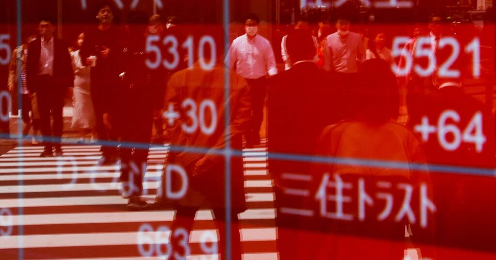 Passersby are reflected on an electric stock quotation board outside a brokerage in Tokyo