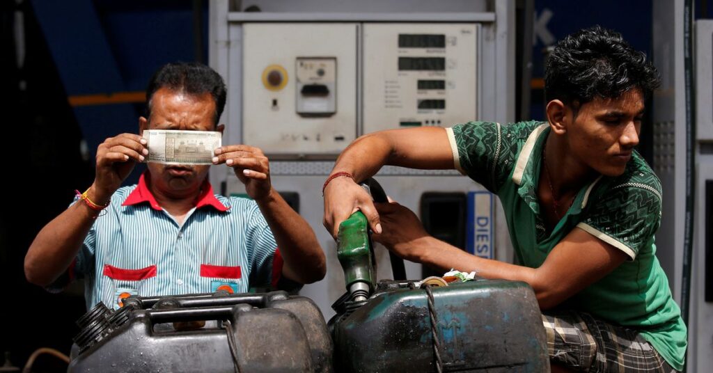 A worker checks a 500 Indian rupee note as a man fills diesel in containers at a fuel station in Kolkata