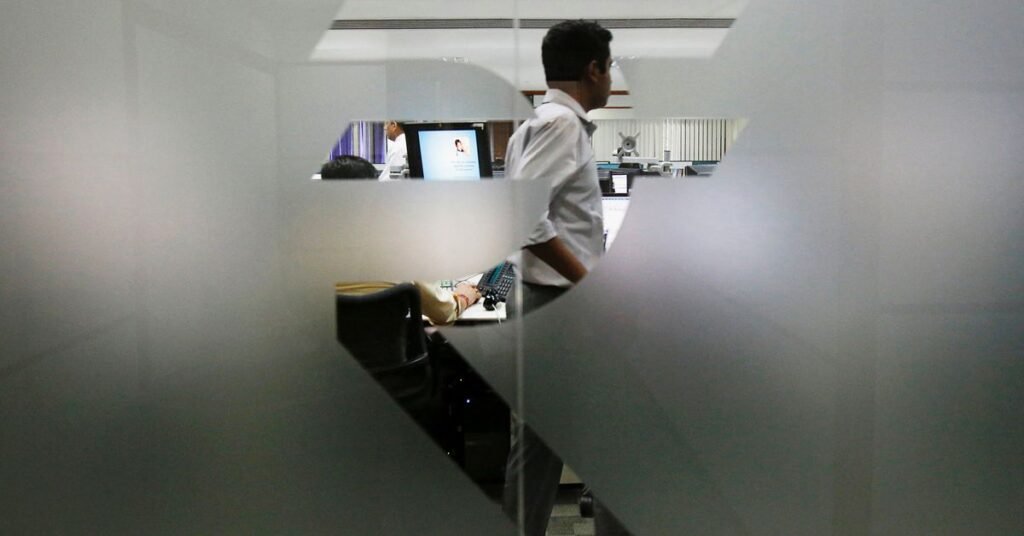A currency trader is pictured through the symbol for the Indian Rupee on the floor of a trading firm in Mumbai