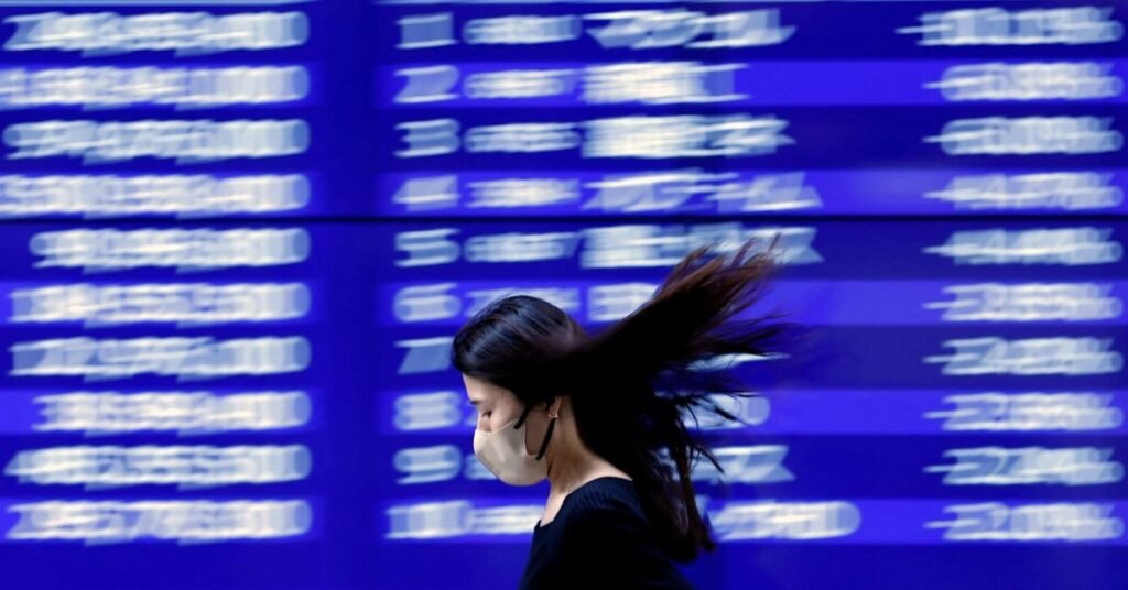الأسهم الآسيوية تتجه نحو الانخفاض، والذهب يقفز مع تراجع النفط A passerby walks past an electric monitor displaying recent movements of various stock prices outside a bank in Tokyo