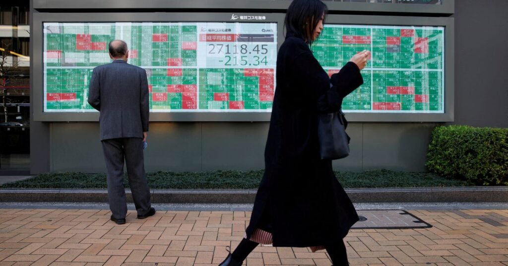 A woman walks past a man examining an electronic board showing Japan