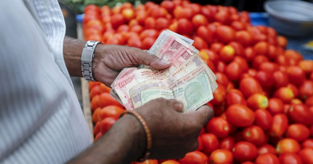 A customer counts money before paying a vegetable vendor at a market in Mumbai