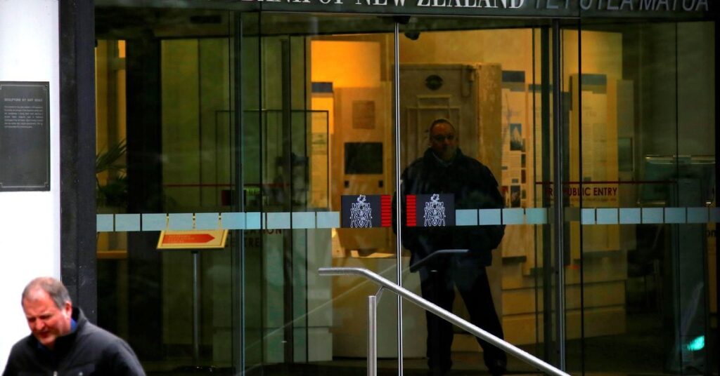 Pedestrians walk past as a security guard stands in the main entrance to the Reserve Bank of New Zealand located in central Wellington, New Zealand